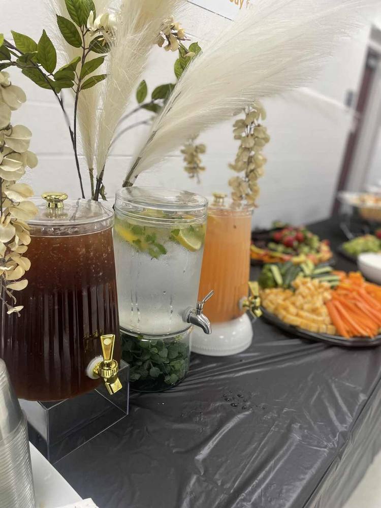 Beverage dispensers styled with soft floral accents beside a catered spread
