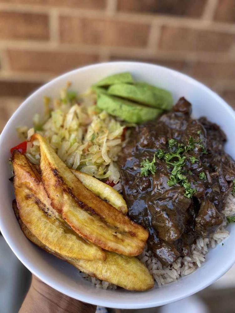 Beef and gravy served over rice with fried plantains, cabbage and avocado
