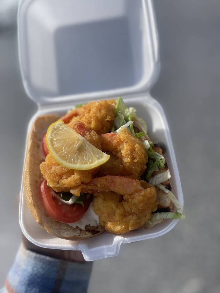 Fried shrimp sandwich with lettuce, tomato and lemon in a takeout box