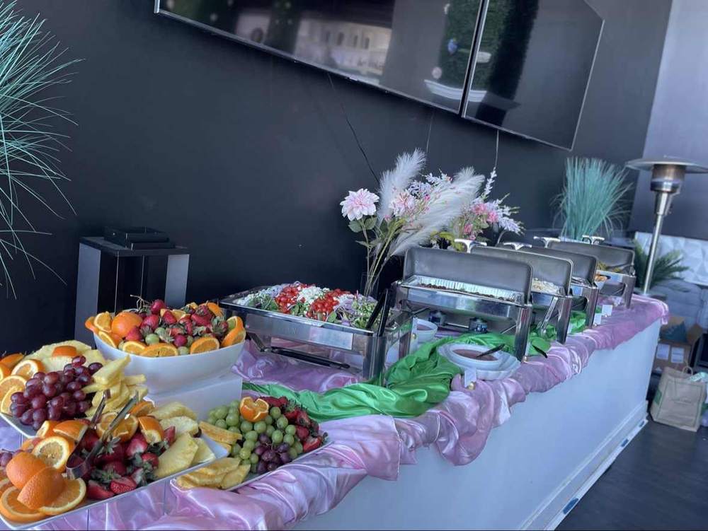 Full pink-and-green catering spread with fruit, salad, chafing dishes and floral accents