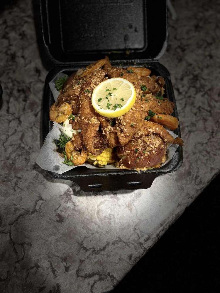 Seafood takeout box piled with seasoned crab legs, shrimp, corn and lemon