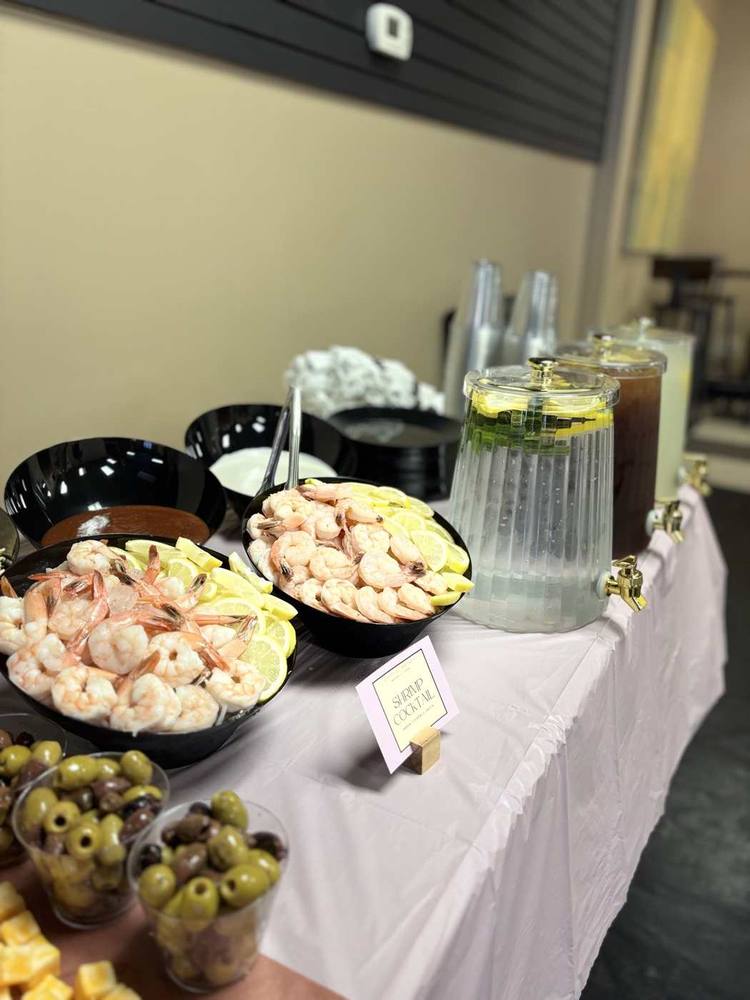 Shrimp cocktail bowls with lemon slices beside chilled beverage dispensers