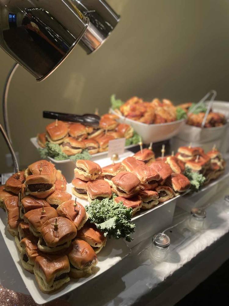 Platters of savory sliders and wings presented under buffet warmers