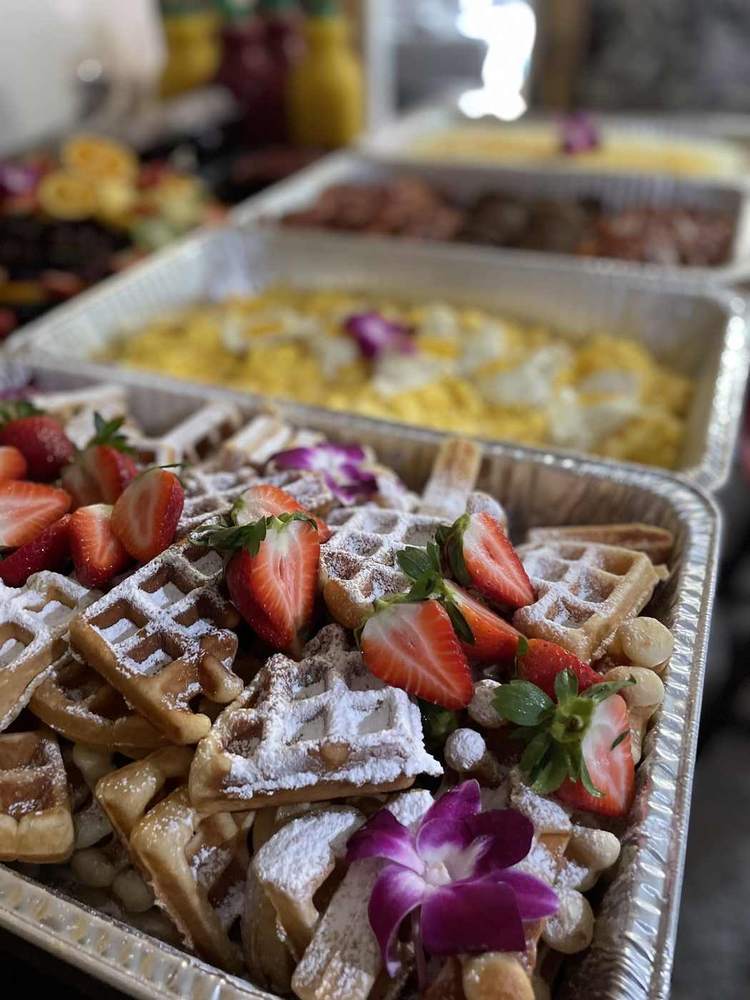 Breakfast buffet with powdered waffles, strawberries, eggs and breakfast meats
