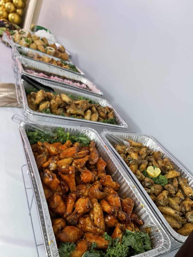Buffet line with trays of sauced wings and seasoned chicken
